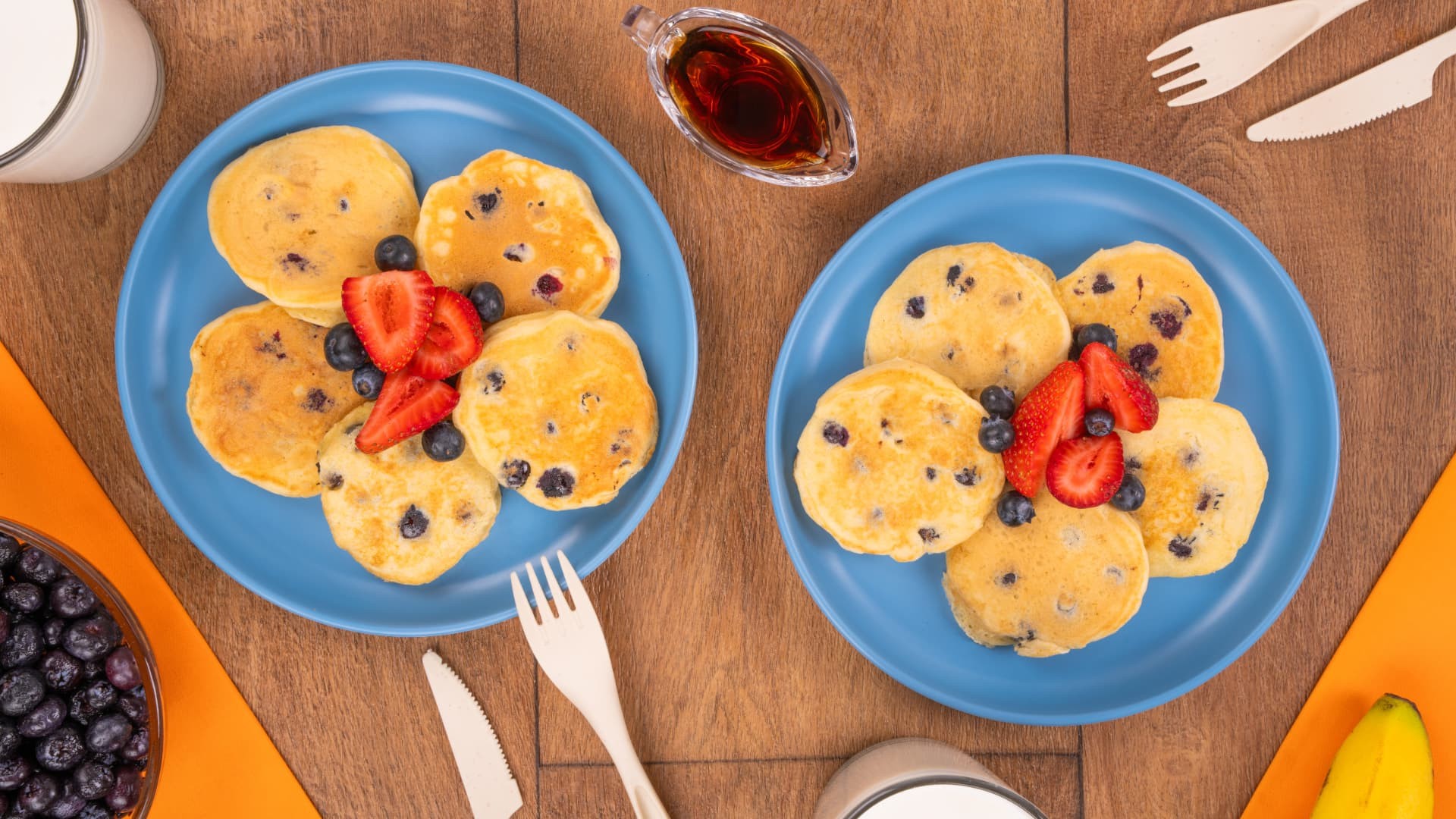 Mini hot cakes de blueberry con fresas y arándanos en platos azules sobre mesa de madera, vista cenital