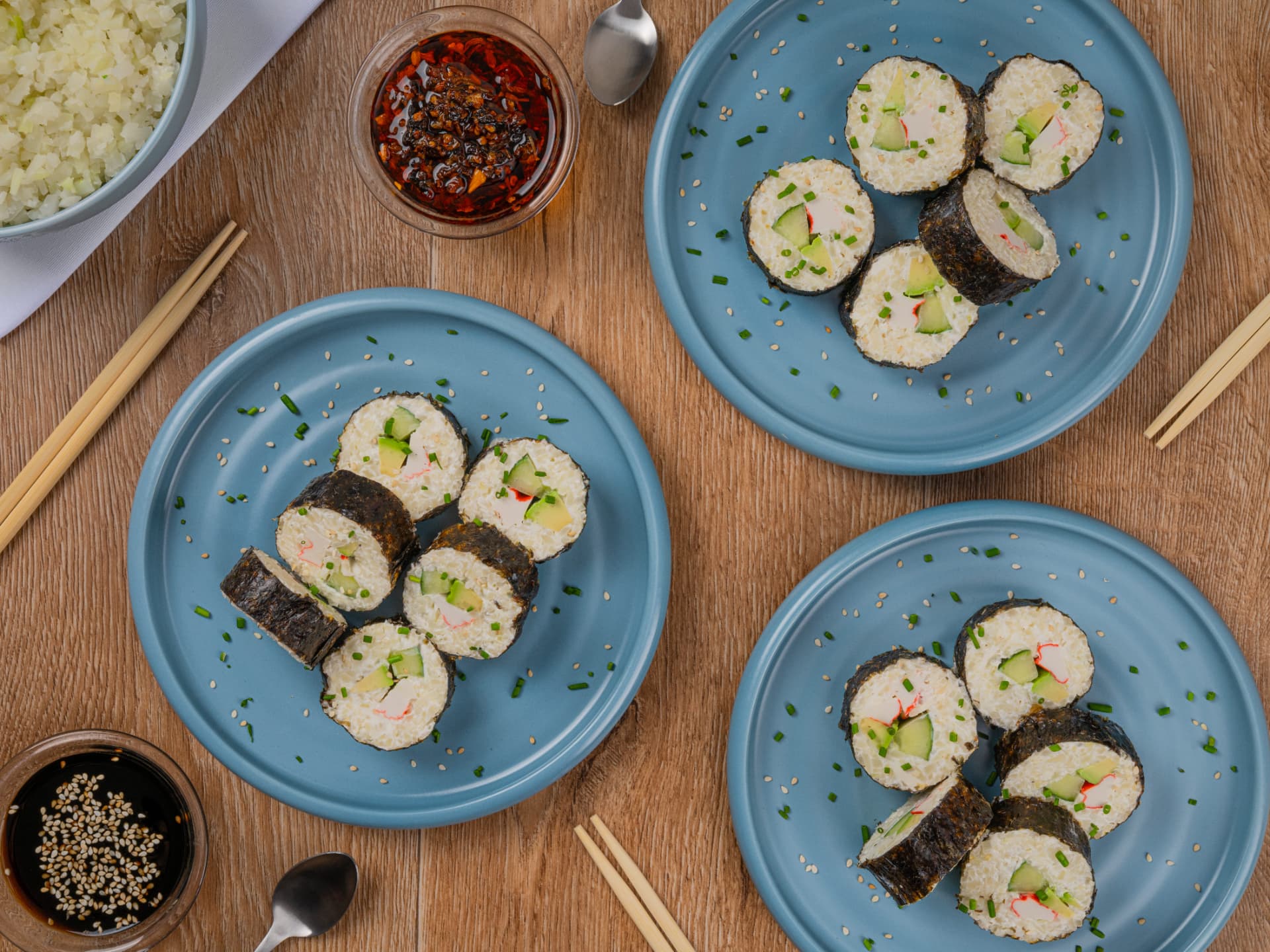 Rollos de sushi de coliflor con surimi en tres platos azules, vista cenital