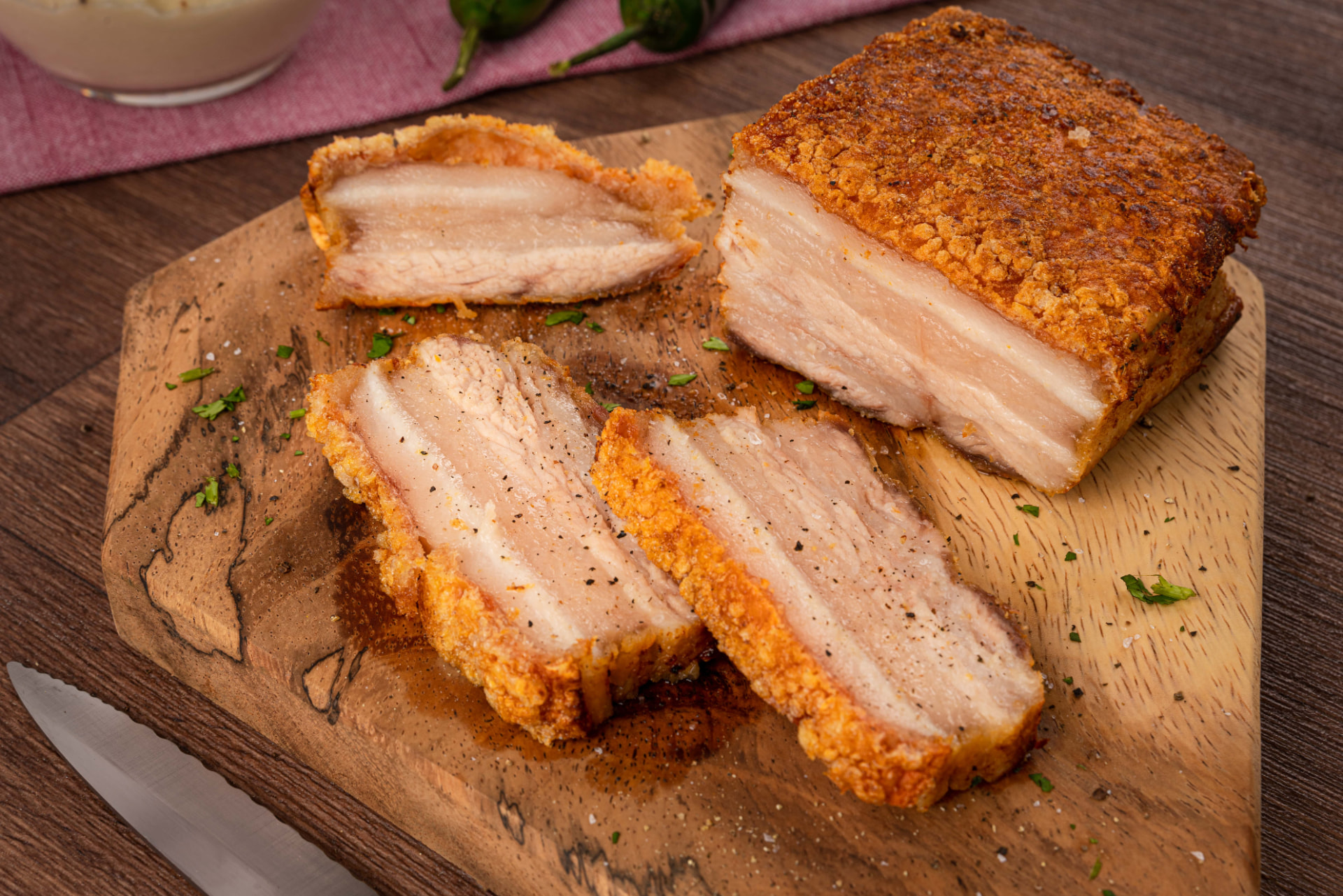 Panceta de cerdo crocante en rebanadas sobre tabla de madera con pimienta y perejil