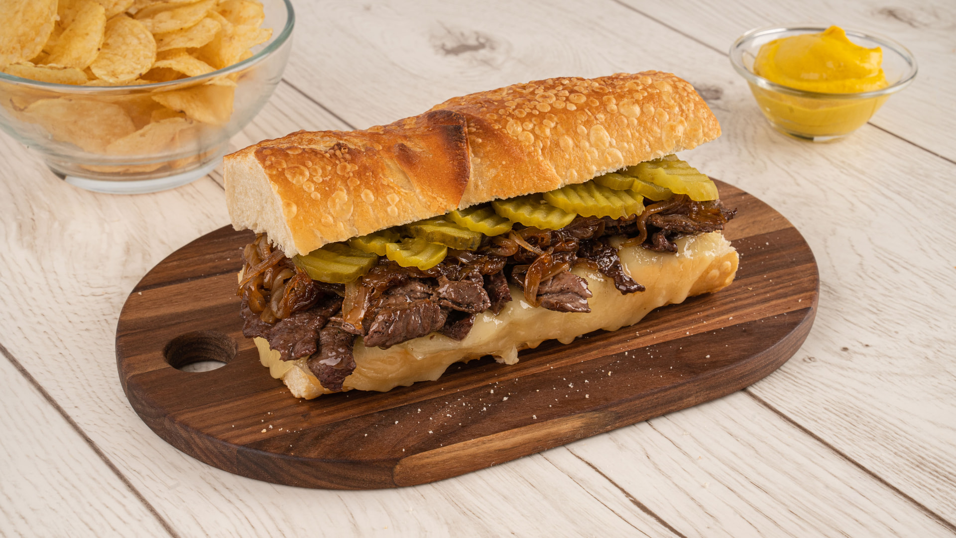 Sándwich de provolone en barra con carne, cebolla y pepinillos sobre tabla de madera, acompañado de papas onduladas y mostaza