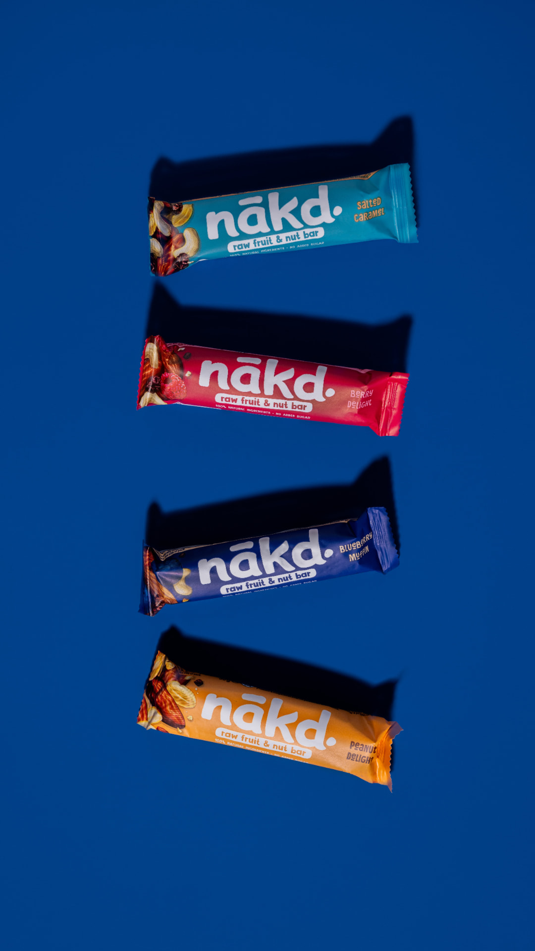 Cuatro barritas de fruta y nuez nakd de distintos sabores sobre fondo azul