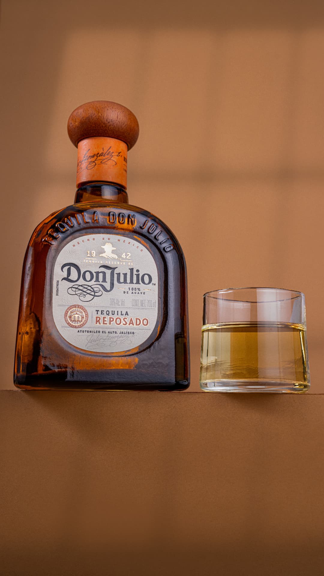 Botella de tequila Don Julio reposado con un vaso sobre fondo cálido